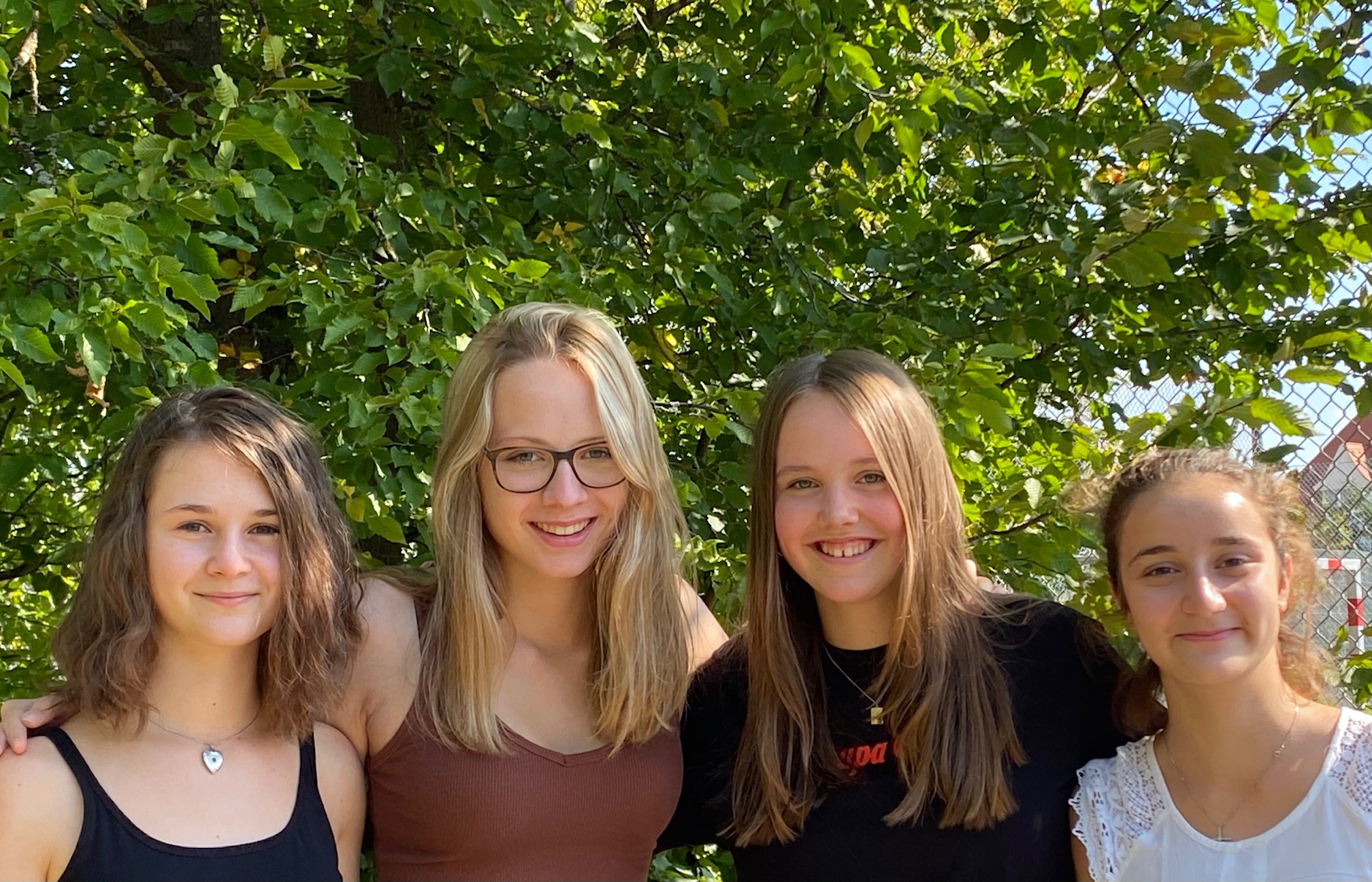 4 blonde jugendliche Mädchen stehen zusammen und lachen