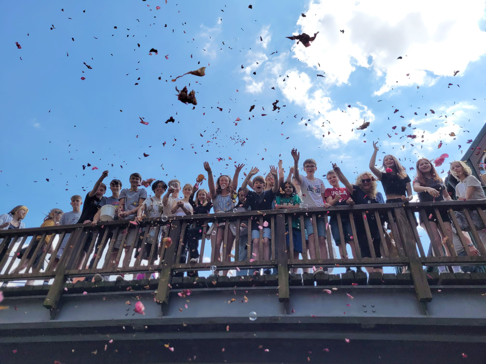 Viele Kinder stehen an einer Brüstung und schmeißen Blütenblätter herunter