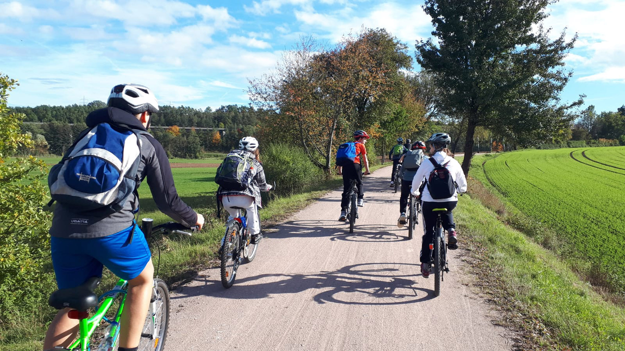 viele Kinder fahren auf Fahrrädern durch eine grüne Landschaft