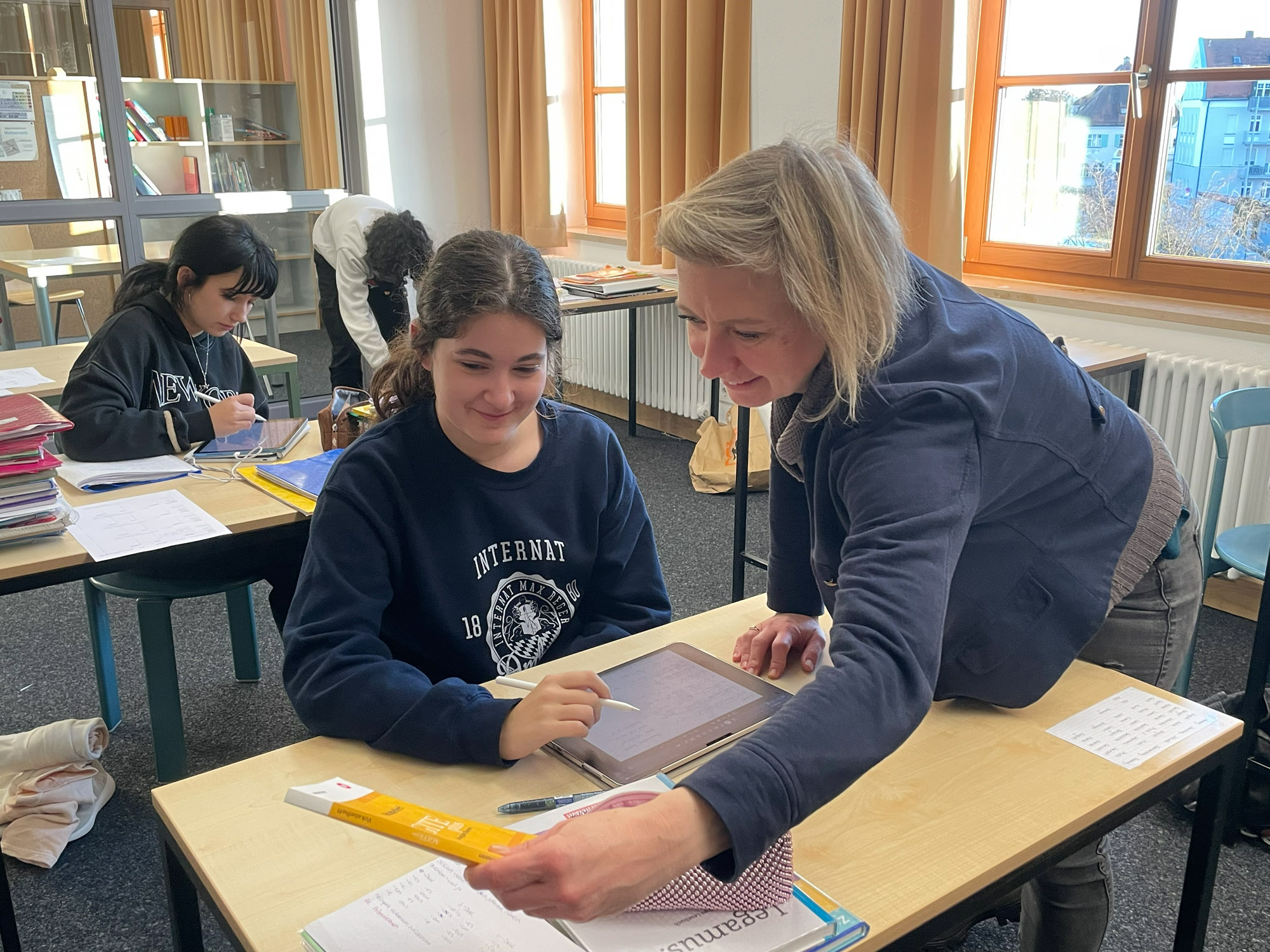 Lehrerin zeigt einem Mädchen ein Buch. Mädchen sitzt am Schreibtisch.
